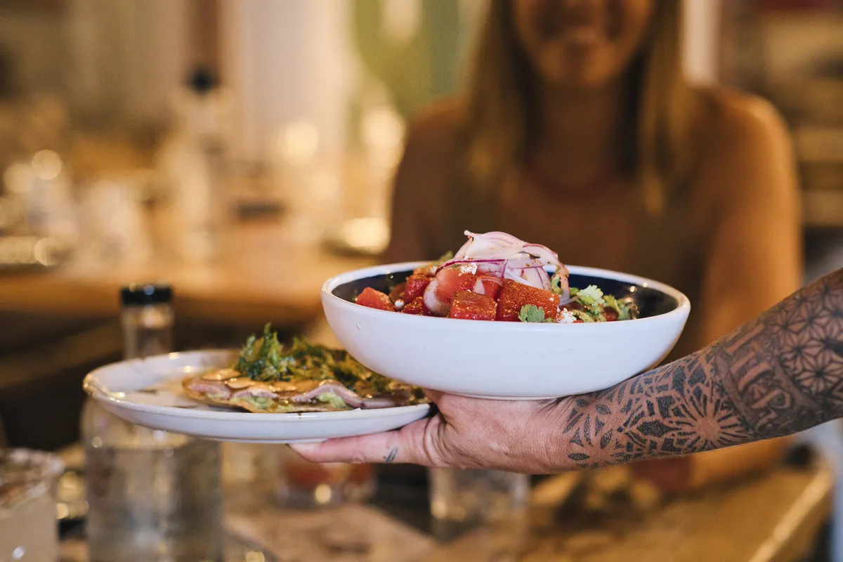 Un cameriere porta al tavolo un ceviche e delle tostadas