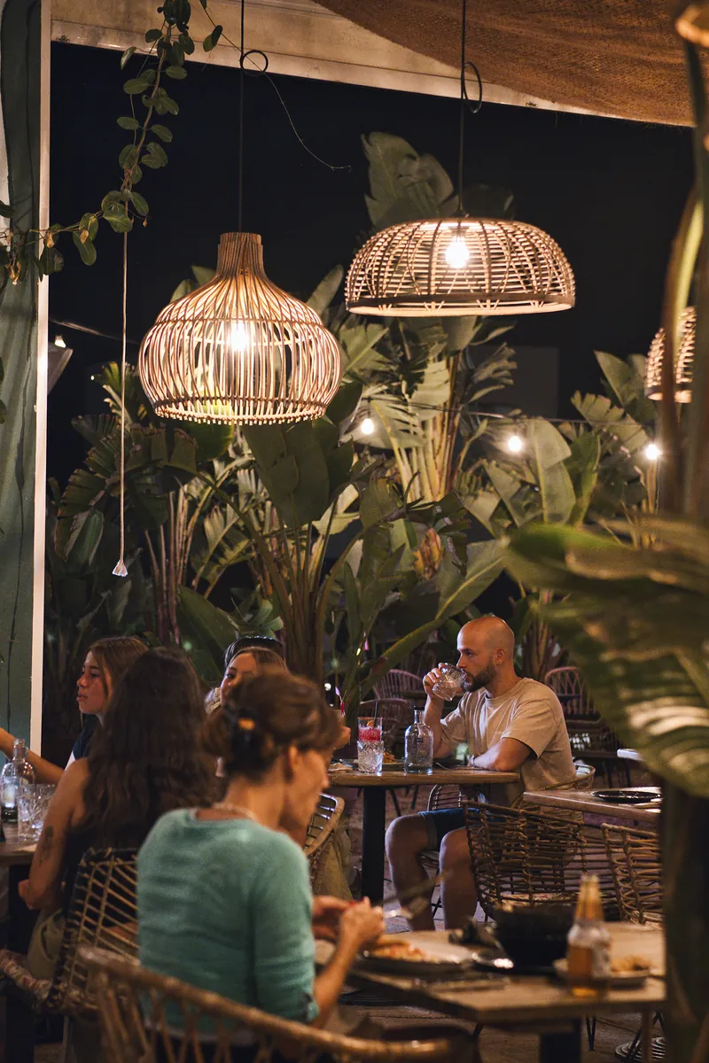 Clientes a jantar sob candeeiros de ratã no terraço