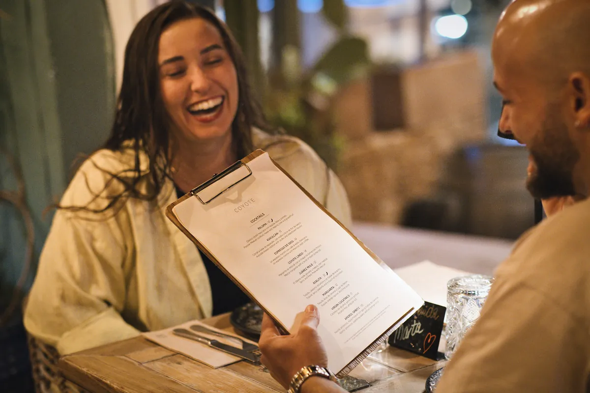 Uma cliente ri à mesa enquanto o seu acompanhante segura a ementa de cócteis